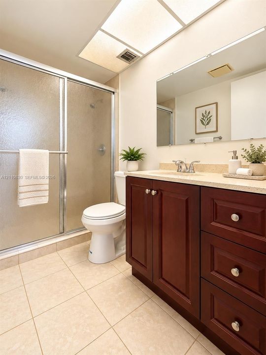 STAGED Bathroom featuring a dark wood-finish vanity with stone-composite countertop, full-width mirror, tile flooring, and a glass-enclosed shower