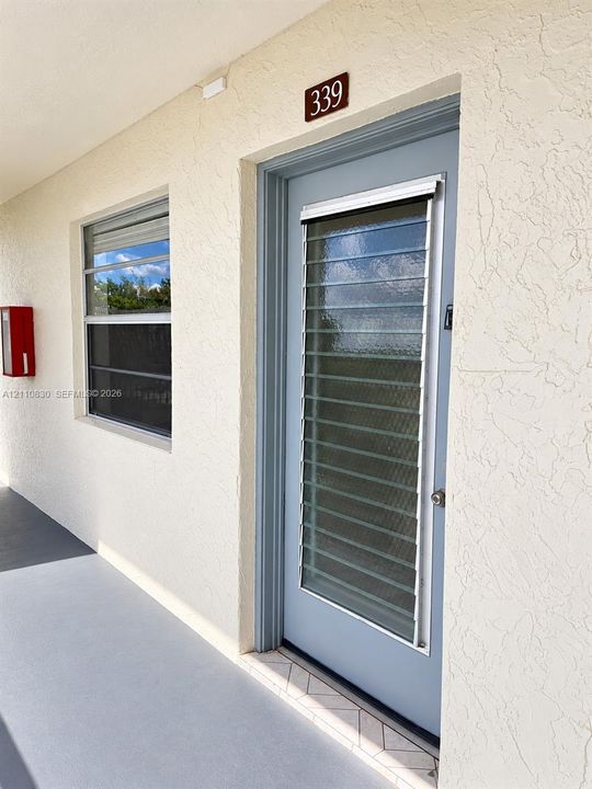 STAGED Textured stucco exterior wall with a blue entry door featuring integrated glass jalousie slats and a metallic door knob