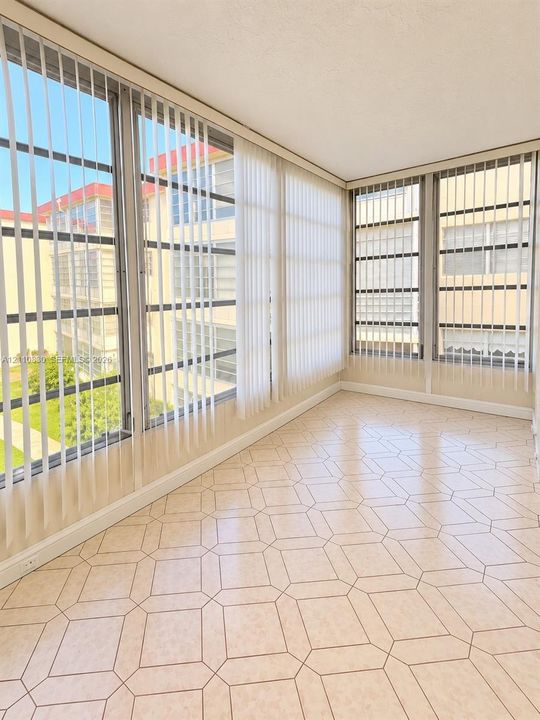 Enclosed space featuring expansive floor-to-ceiling windows, geometric-patterned tile flooring, and vertical blinds