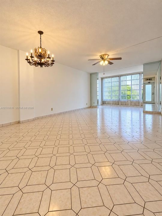 Spacious interior featuring patterned tile flooring, a multi-arm candelabra-style chandelier, a ceiling fan with integrated lighting, and floor-to-ceiling windows with vertical blinds
