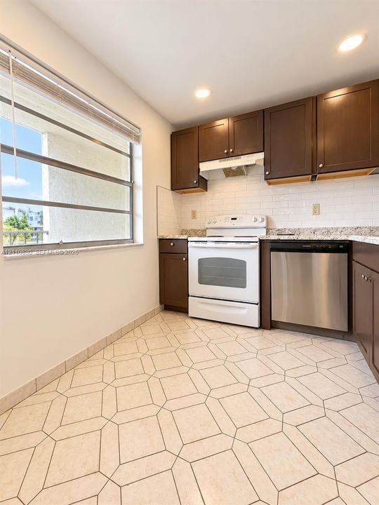 Kitchen featuring dark cabinetry, stone-finish countertops, subway tile backsplash, stainless steel dishwasher, and geometric tile flooring