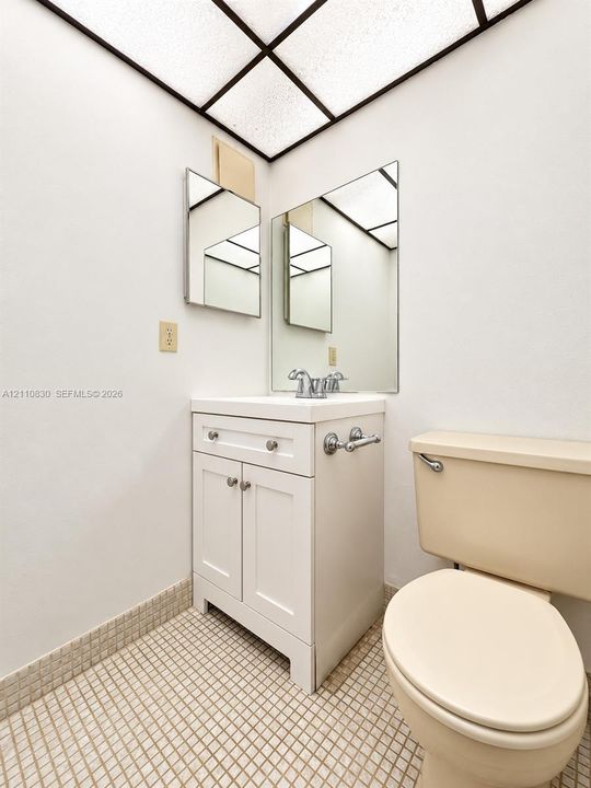 White shaker-style vanity with a square sink, chrome-finish dual-handle faucet, grid-pattern ceiling light, and mosaic-tiled flooring