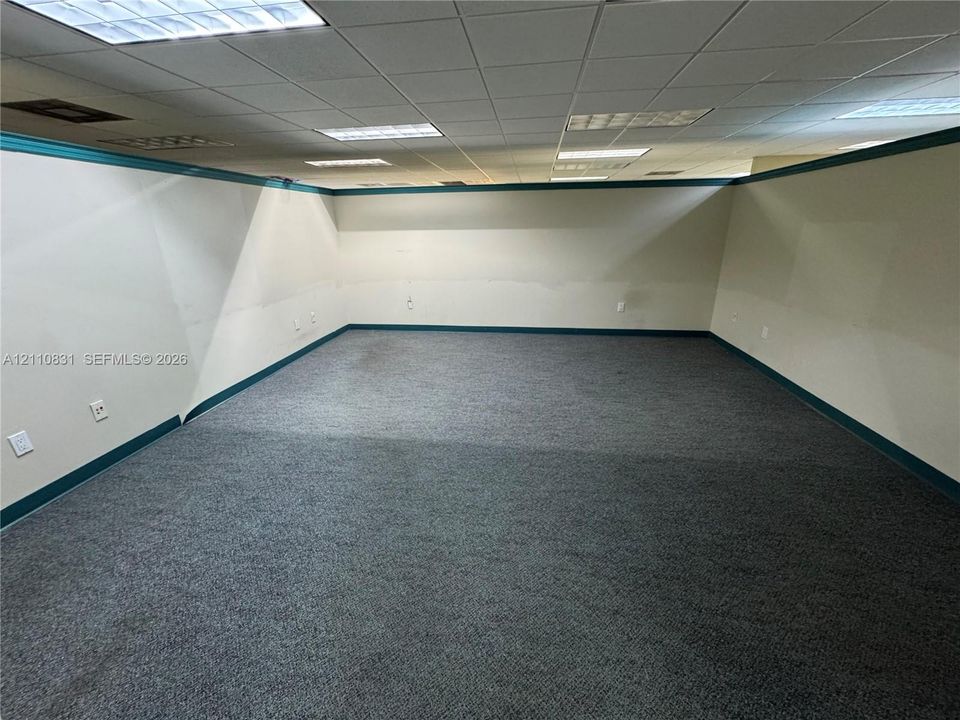 Interior room featuring wall-to-wall carpeting, a drop ceiling with recessed lighting panels, and painted walls with decorative trim