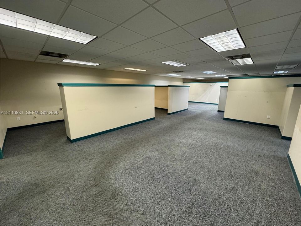 Expansive open-concept interior featuring wall-to-wall carpeting, drop ceiling tiles, recessed grid lighting, and partial-height privacy partitions with decorative trim