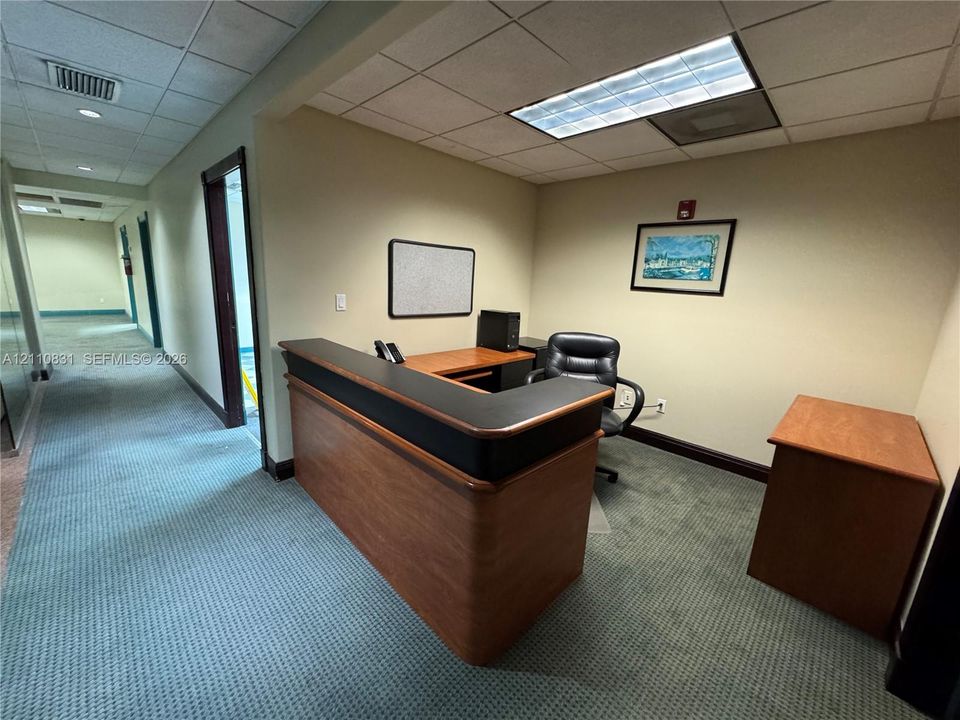Built-in wood-finish reception desk with contrasting black laminate top, recessed acoustic tile ceiling, and carpeted flooring