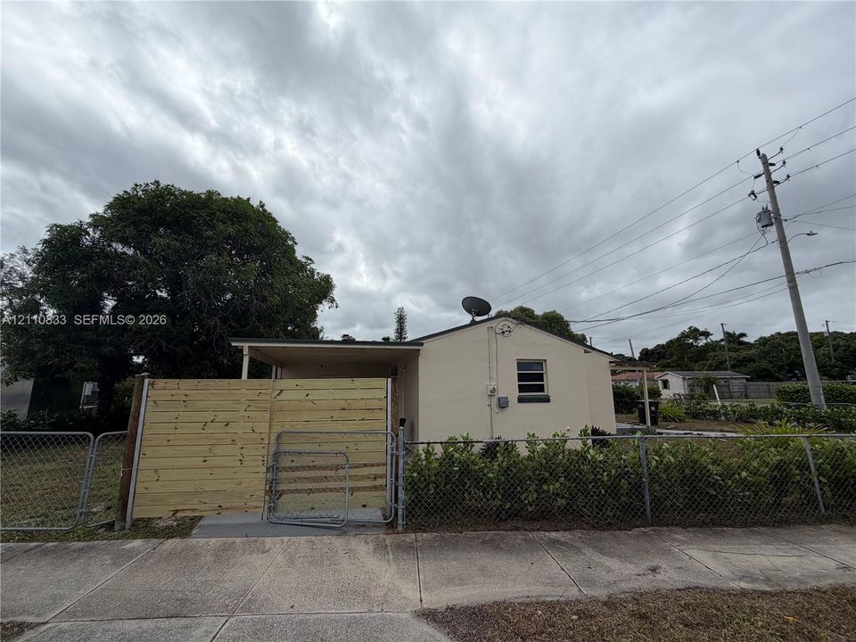 Stucco exterior with a covered side porch, horizontal wood-slat privacy fencing, and chain-link perimeter fencing