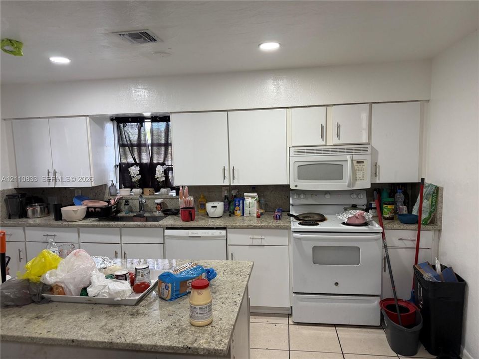 Kitchen featuring white cabinetry, stone-finish countertops, a stone-finish island, tile flooring, and built-in appliances