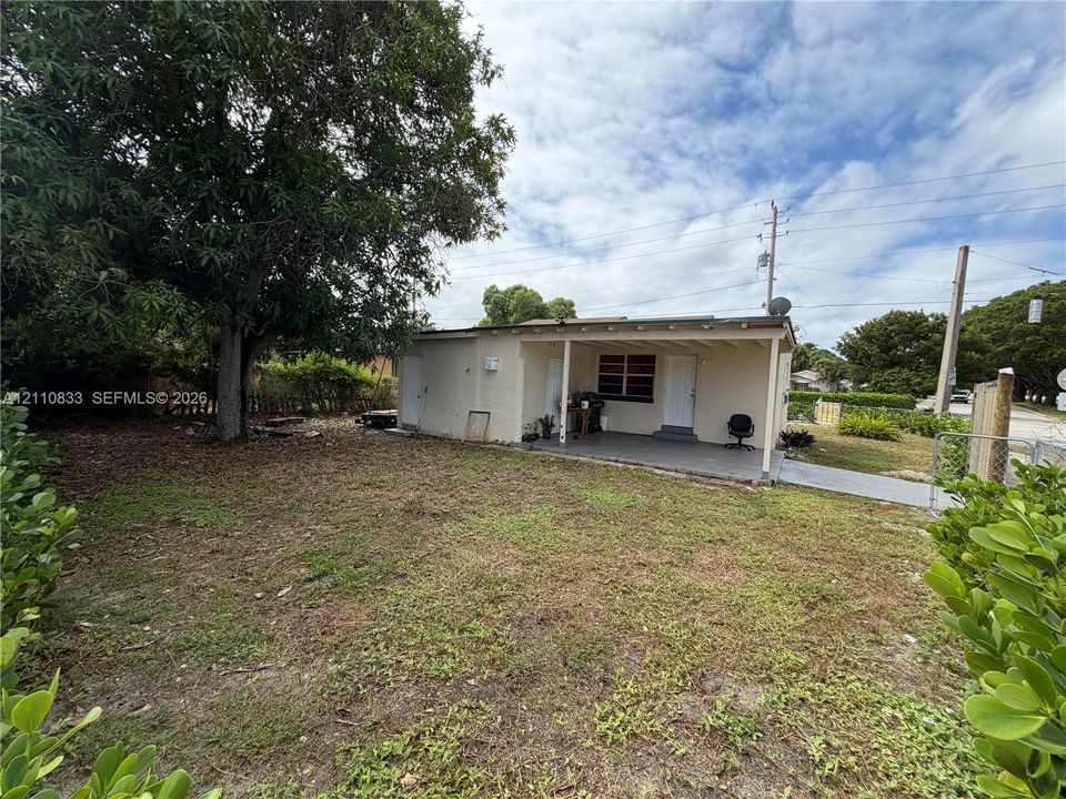 Exterior property featuring a covered patio, concrete walkway, and mature trees situated on a parcel with perimeter fencing