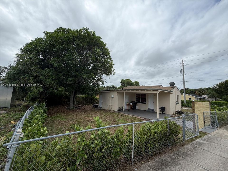 Single-story residence featuring a covered front porch, chain-link perimeter fencing, and a mature tree