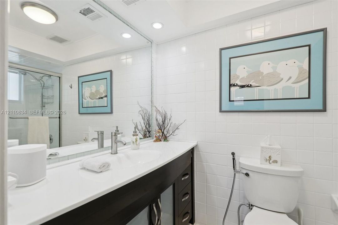Bathroom vanity featuring a solid surface countertop, integrated sink, dark-toned cabinetry, full-width mirror, and shower enclosure with a glass door