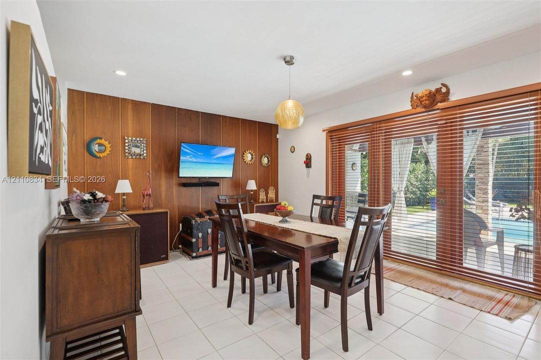 Dining area featuring white tile flooring, wood-paneled accent wall, recessed lighting, spherical pendant light, and sliding glass doors with wood blinds