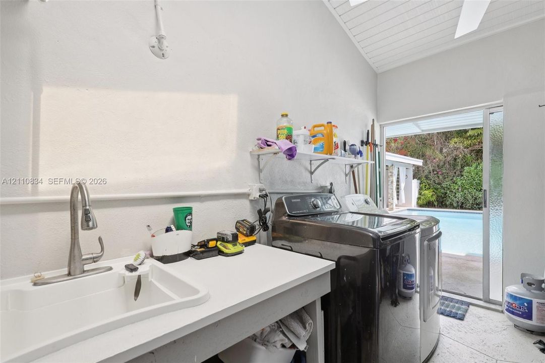 Laundry area featuring a utility sink with a high-arch pull-down faucet, vaulted ceiling with tongue-and-groove finish, tile flooring, and glass sliding door access to the exterior pool area