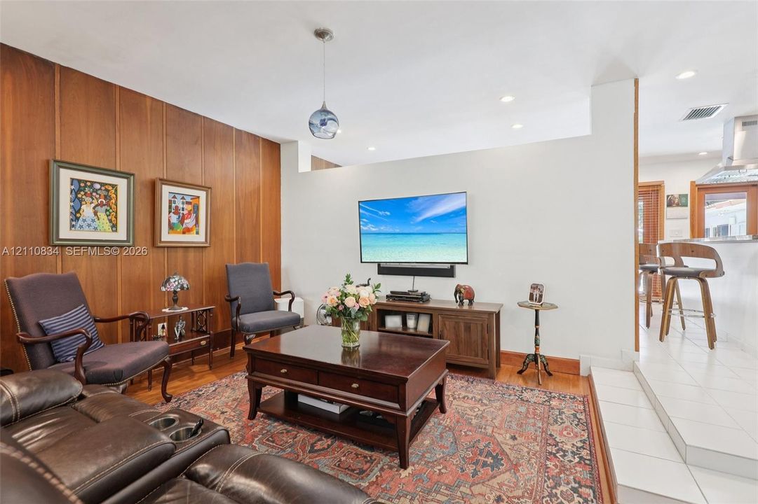 Wood-paneled accent wall, recessed lighting, glass pendant fixture, hardwood flooring, and tiered floor elevation