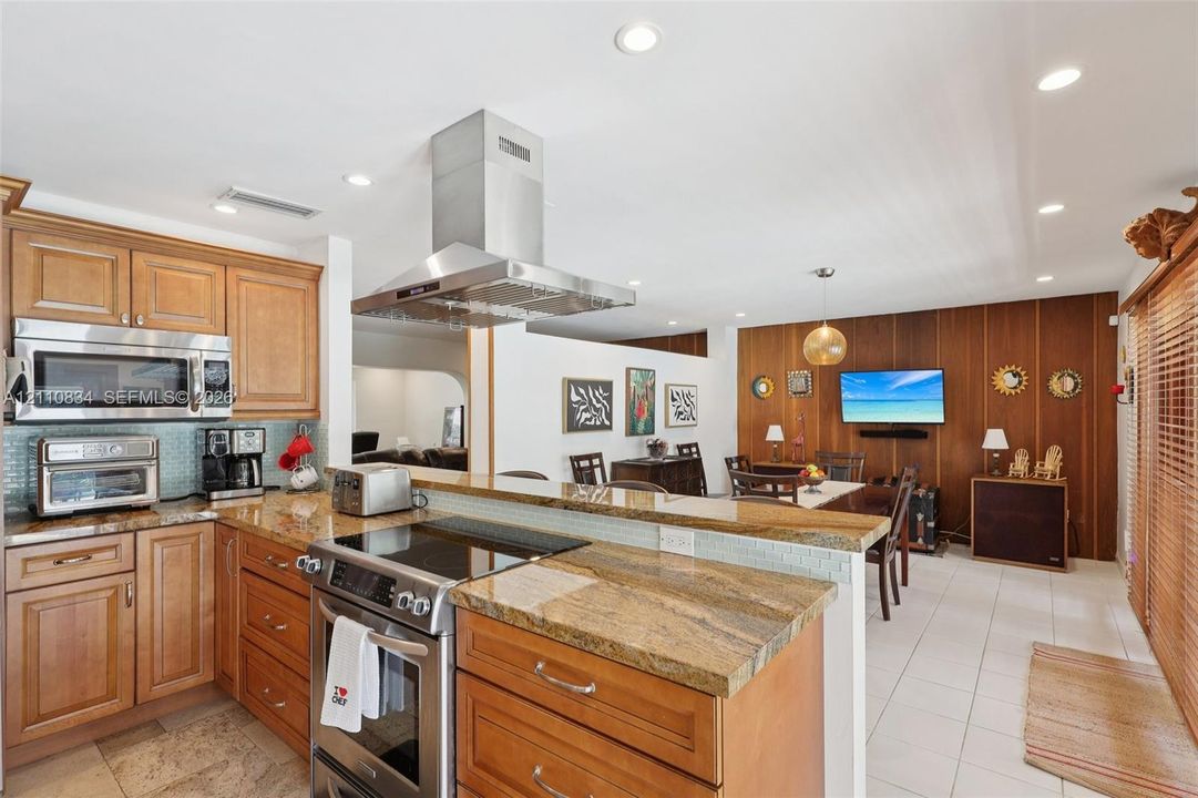Kitchen featuring wood cabinetry, stone countertops, stainless steel range with overhead vent hood, built-in microwave, and tile flooring