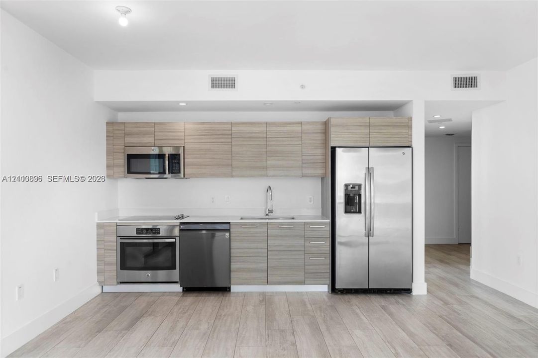 Kitchen featuring wood-finish cabinetry, stainless steel appliances, a flat-top range, and light-toned wood-finish flooring