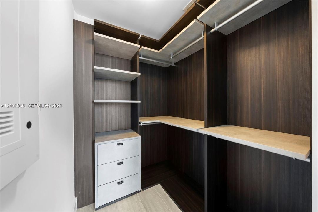 Custom walk-in closet featuring dark wood-finish cabinetry, built-in open shelving, tiered hanging rods, and integrated three-drawer storage