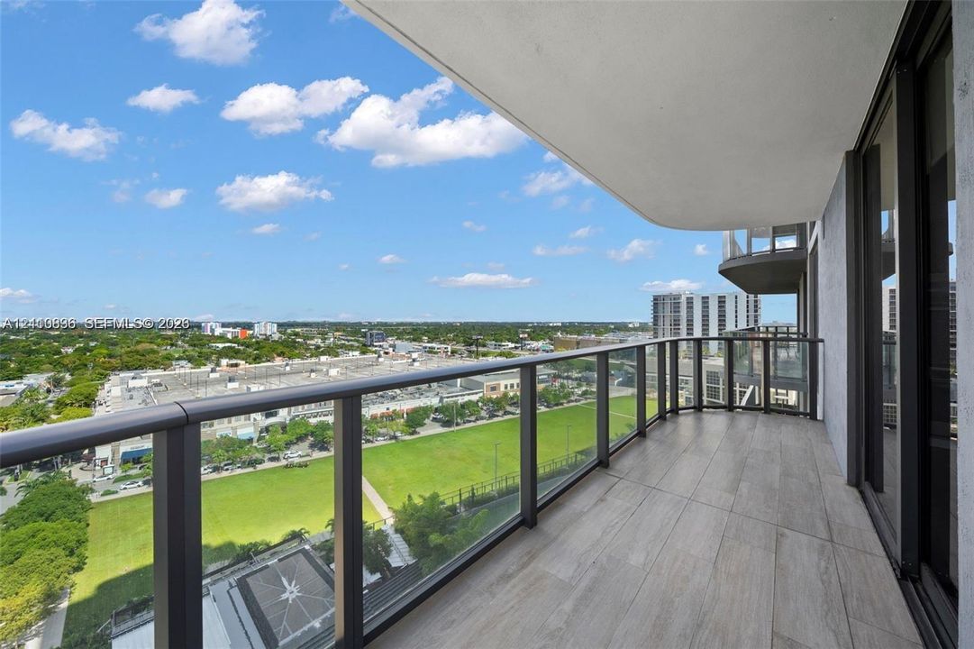 Covered balcony featuring wood-finish tile flooring and a glass-panel railing with metal frame