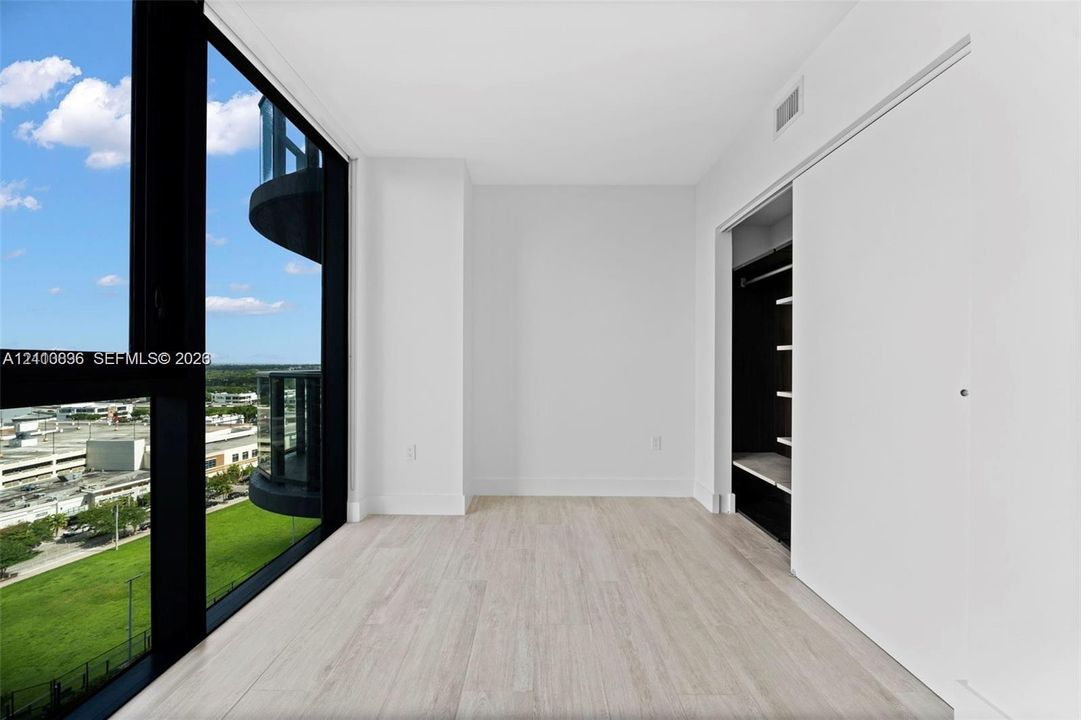 Floor-to-ceiling windows, wood-finish flooring, and a built-in closet with sliding doors