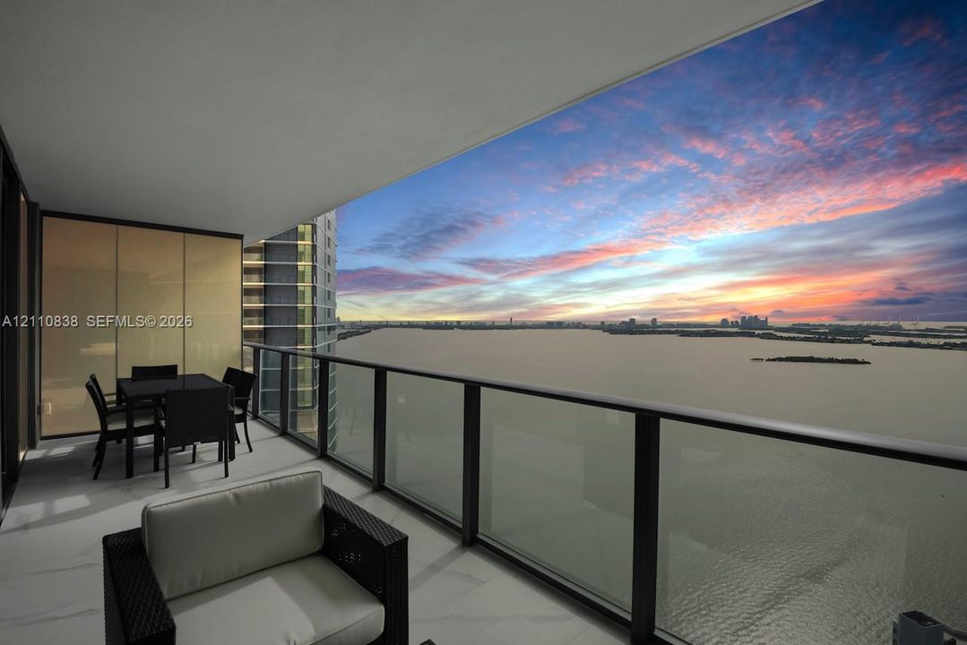 Covered balcony with a glass railing, large-format tile flooring, and expansive water backdrop