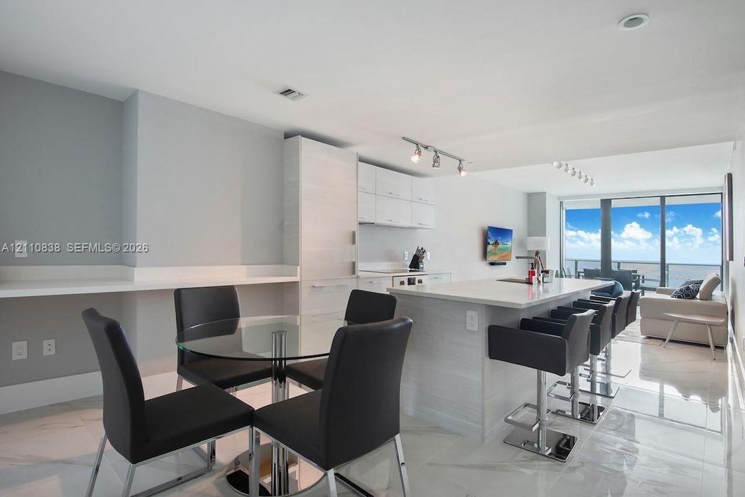 Open-concept kitchen featuring horizontal-grain cabinetry, stone-surfaced center island, polished flooring, track lighting, and floor-to-ceiling glass windows