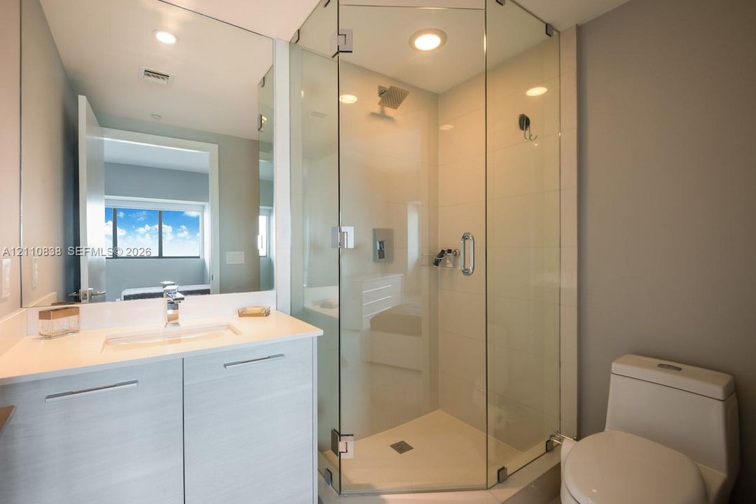 Corner shower enclosure with frameless glass panels, floating vanity with solid-surface countertop, integrated sink, and full-width vanity mirror