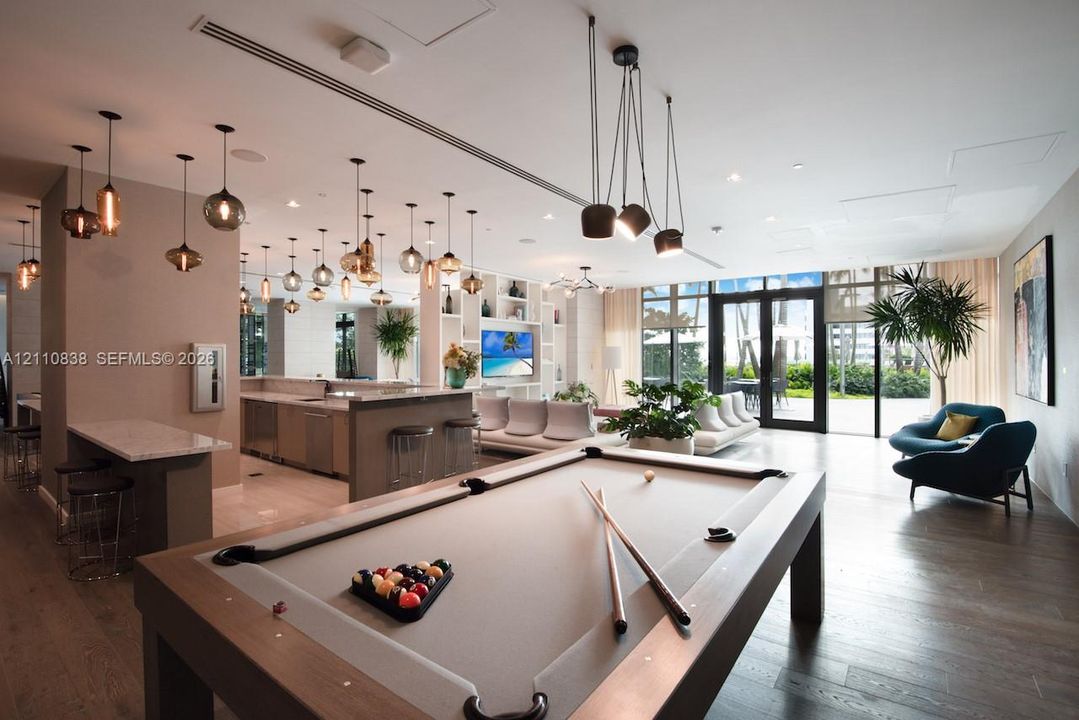 Open-concept interior featuring wood-finish flooring, built-in shelving, a wet bar with stone-surfaced countertops, custom multi-pendant lighting, and floor-to-ceiling glass doors