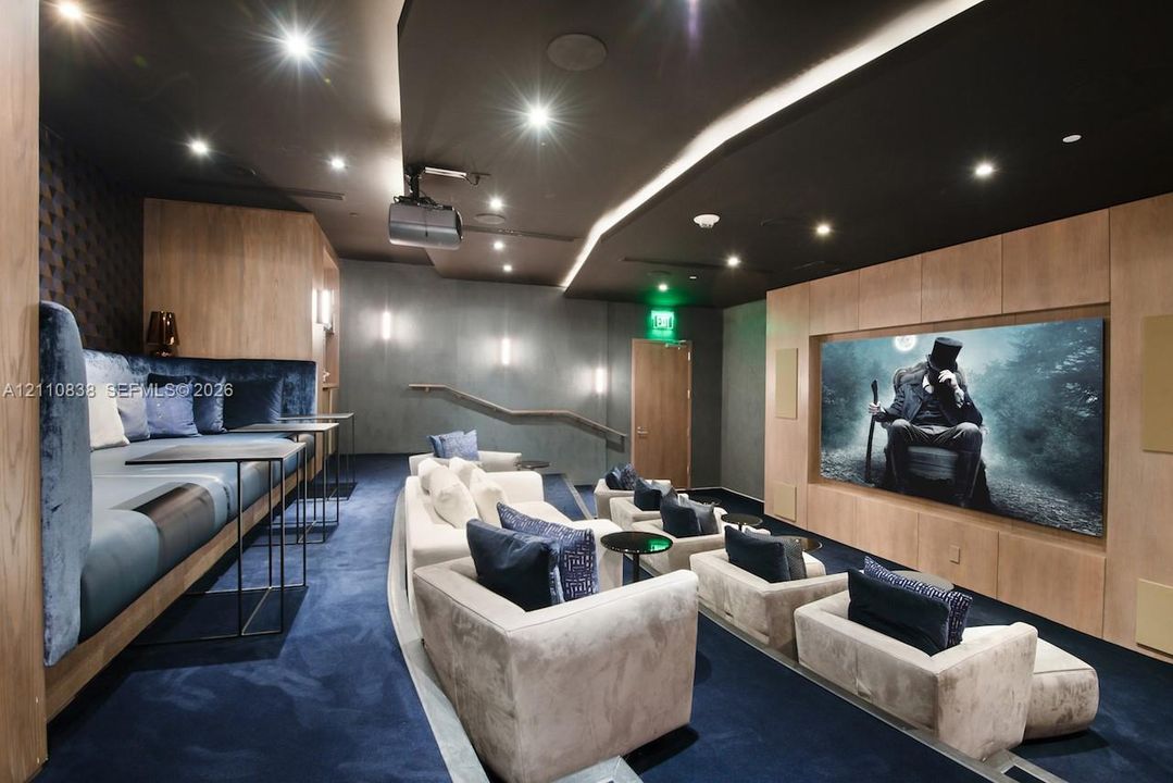 Media room featuring built-in wood-paneled wall cabinetry, tiered floor levels, recessed ceiling lighting, and integrated wall sconces
