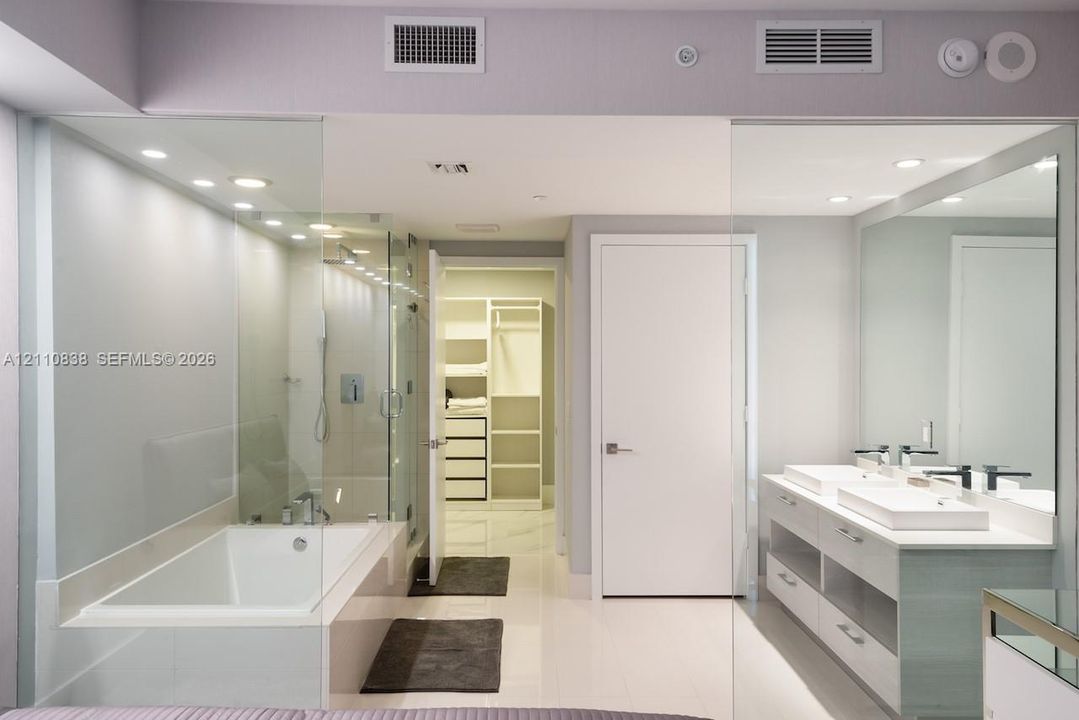 Double vanity with rectangular vessel sinks, frameless glass-enclosed soaking tub and shower, recessed ceiling lighting, and built-in closet organization system