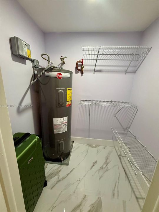 Utility space featuring large-format tile flooring, a Rheem water heater, and wall-mounted wire shelving