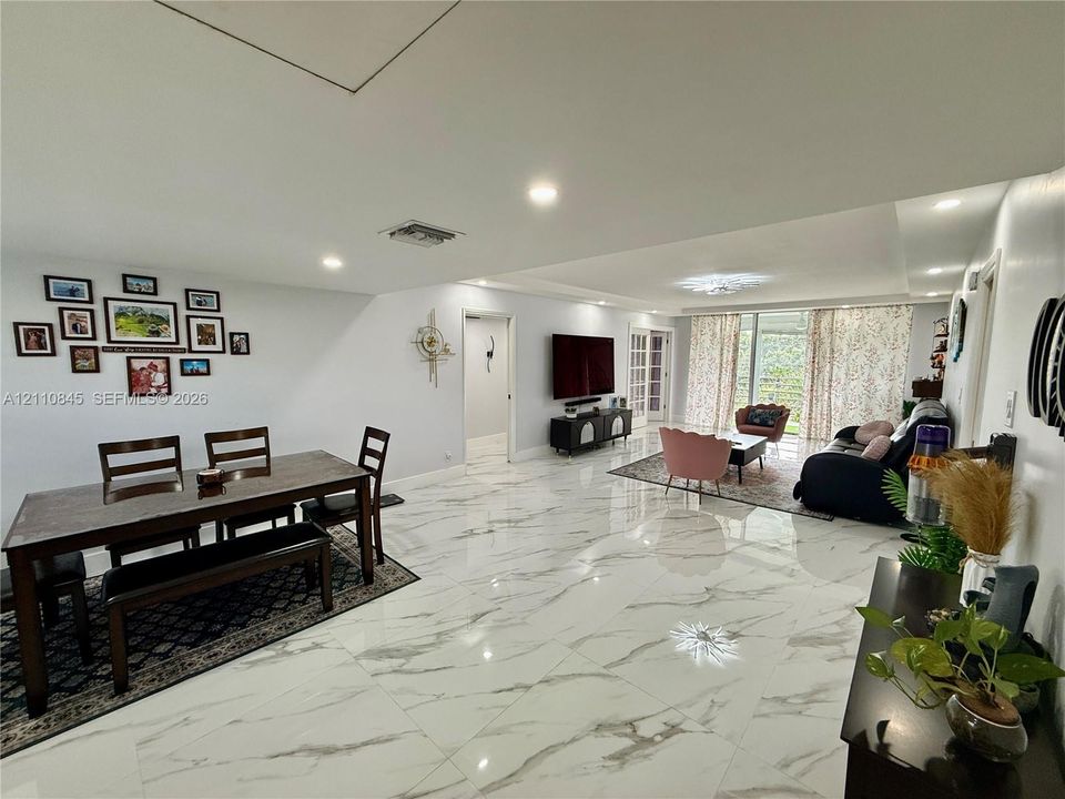Open-concept interior featuring large-format polished stone-finish flooring, recessed lighting, and expansive glass pane doors leading to exterior space
