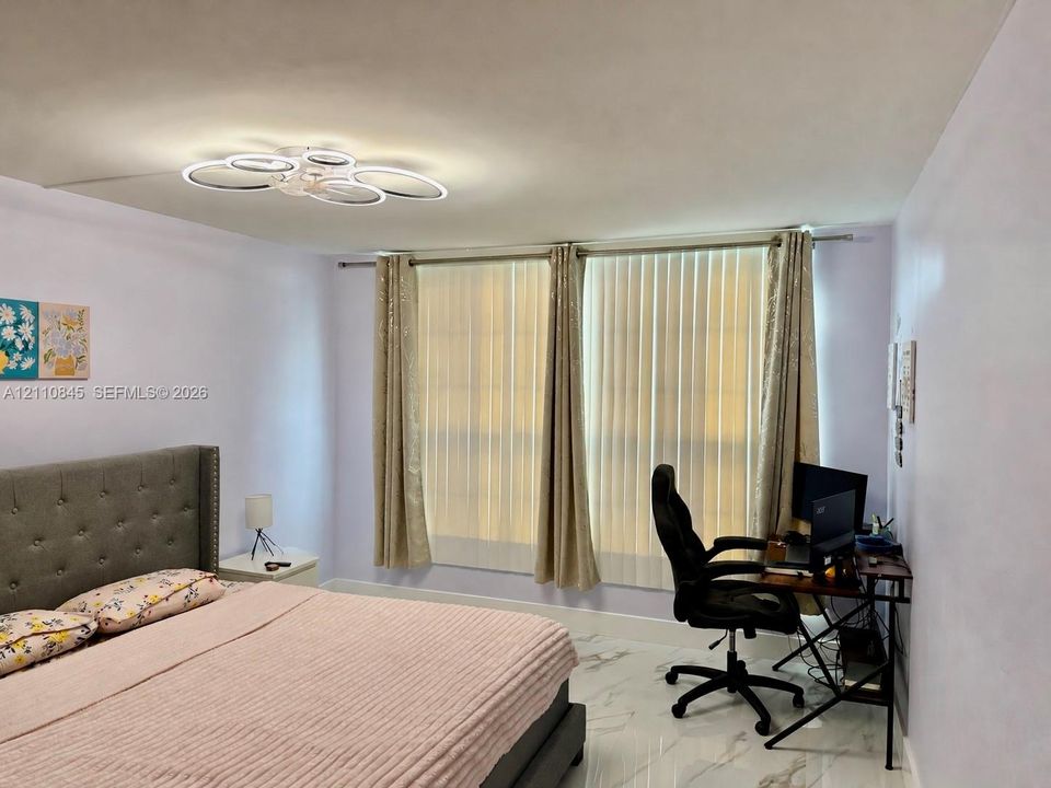 Interior space featuring polished white tile flooring with grey veining, a modern multi-ring LED flush-mount light fixture, and floor-to-ceiling vertical blinds