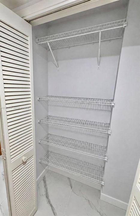Storage area featuring louvered bi-fold doors, four-tier ventilated wire shelving, and stone-finish flooring