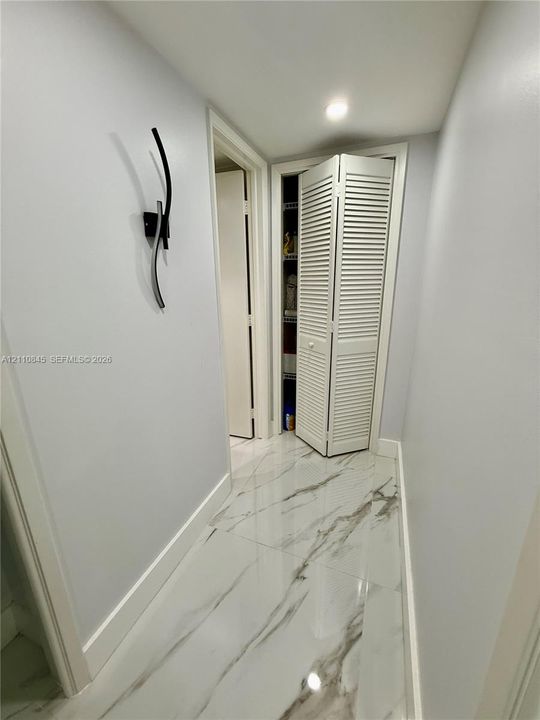 Large-format tile flooring with a neutral-toned veined pattern, louvered bi-fold closet doors, and a contemporary wall-mounted light fixture