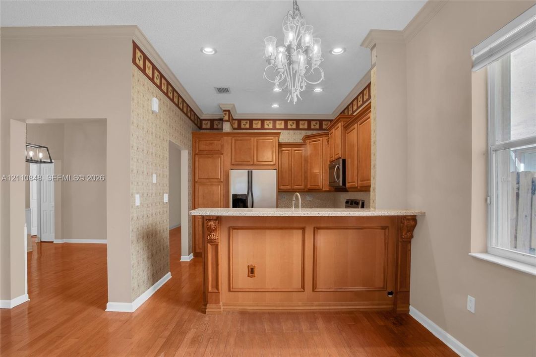 Kitchen featuring wood-finish cabinetry, a raised breakfast bar with stone-surfaced countertop, recessed lighting, and a decorative chandelier