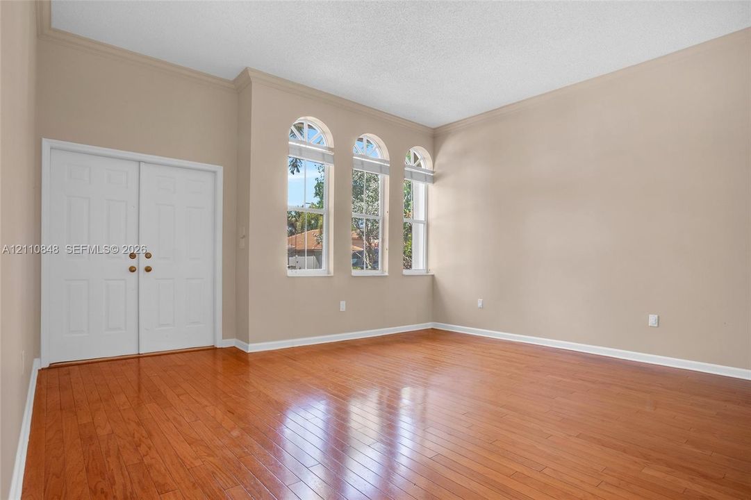 High-ceiling interior featuring wood-finish flooring, triple arched windows, and double-door entry