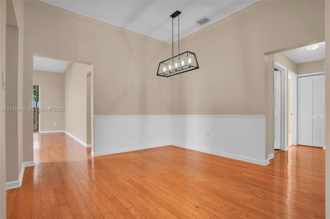 Wood-finish flooring, half-wall wainscoting, and a linear cage-style chandelier