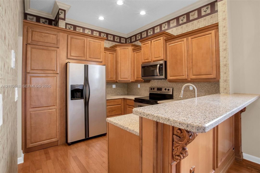 Kitchen featuring wood cabinetry, stone-finish countertops, stainless steel appliances, recessed lighting, and wood-finish flooring
