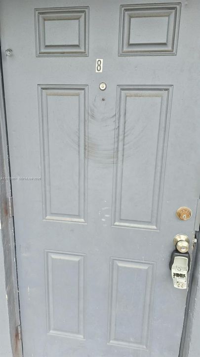 Grey-painted six-panel entry door featuring a brass-finished knob, deadbolt, and mounted door viewer