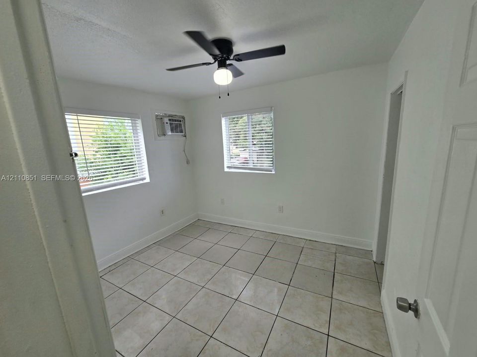 Room featuring neutral tile flooring, dual windows with horizontal blinds, and a ceiling-mounted light fixture with fan
