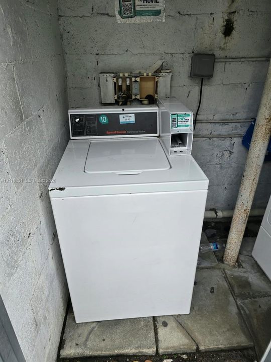 Commercial-grade top-load washing machine featuring a built-in coin-operated payment module and exposed concrete block masonry wall