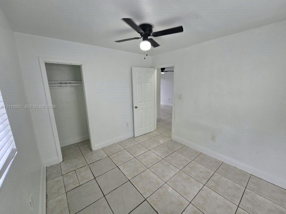 Room featuring light-toned tile flooring, a matte black ceiling fan with an integrated light fixture, a six-panel interior door, and a built-in closet with an overhead shelf