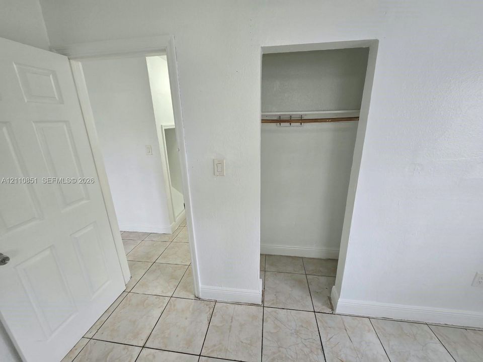 Interior space featuring ceramic tile flooring, a six-panel door, and a built-in closet with a shelf and hanging rod