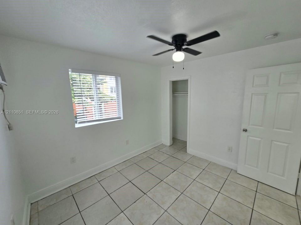 Room featuring tile flooring, a window with horizontal blinds, a ceiling fan with light fixture, a closet, and a six-panel door