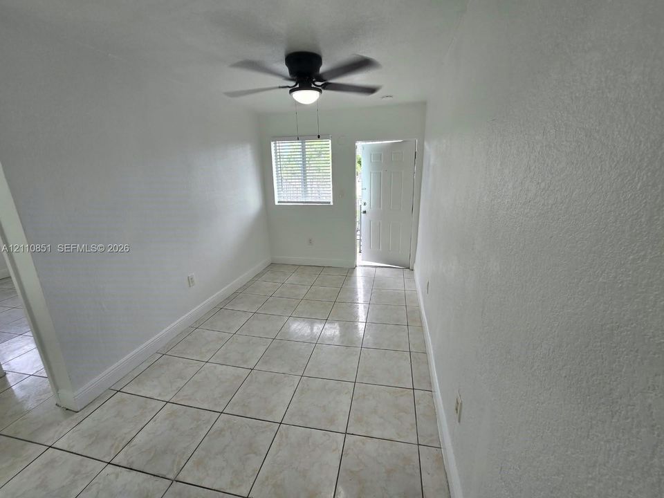 Neutral-toned tiled flooring, white walls, integrated ceiling fan with light fixture, and horizontal blinds