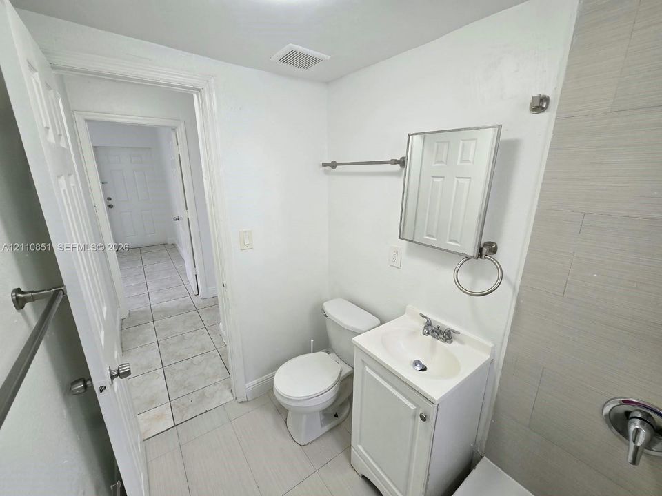 Bathroom featuring large-format tile flooring, a white vanity with an integrated basin, a mirrored medicine cabinet, and light-toned wall tile surrounding the shower area