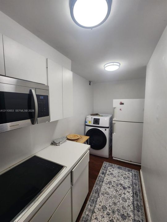 White cabinetry, solid-surface countertops, built-in stainless steel microwave, integrated electric cooktop, and wood-finish flooring