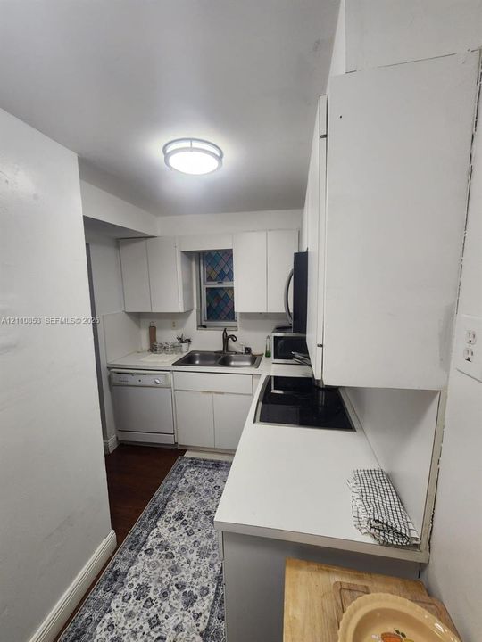 Kitchen featuring white cabinetry, solid-surface countertops, dual-basin stainless steel sink, black glass cooktop, and built-in dishwasher