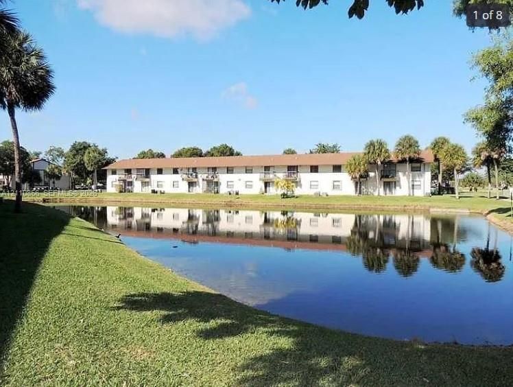Multi-story building featuring a pitched shingle roof, balconies, exterior staircases, and a landscaped waterfront setting with mature palm trees