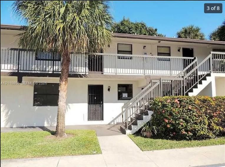 Two-story exterior featuring white stucco siding, metal railing systems, exterior staircases, and mature palm landscaping
