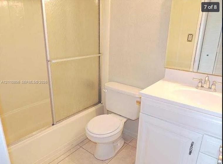 Bathroom featuring a white vanity cabinet with an integrated sink, polished metal faucet, tiled flooring, and a tub-shower combination with a sliding glass enclosure